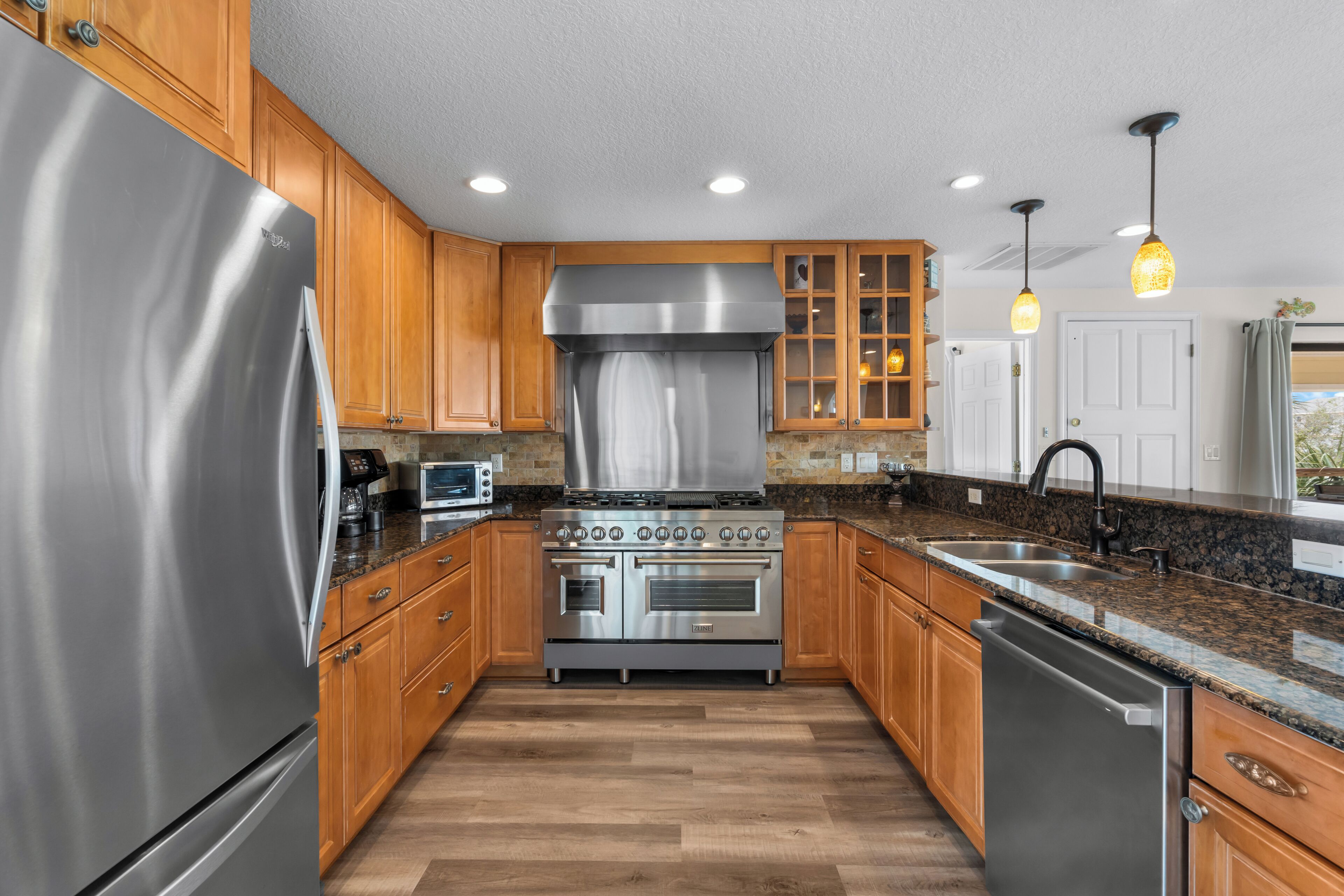 Una cocina con armarios de madera, electrodomésticos de acero inoxidable, encimeras de granito e iluminación colgante.