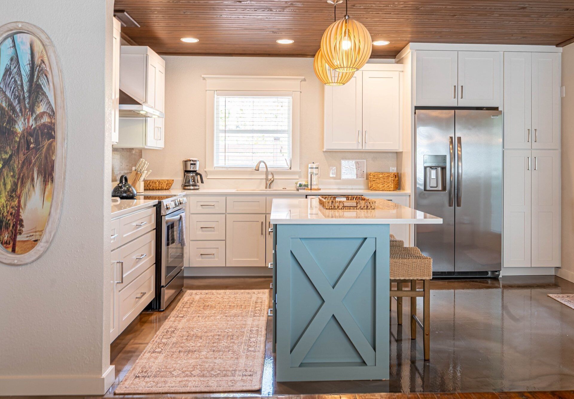 A modern kitchen with white cabinets, a central island, a stainless steel refrigerator, and a hanging light fixture.