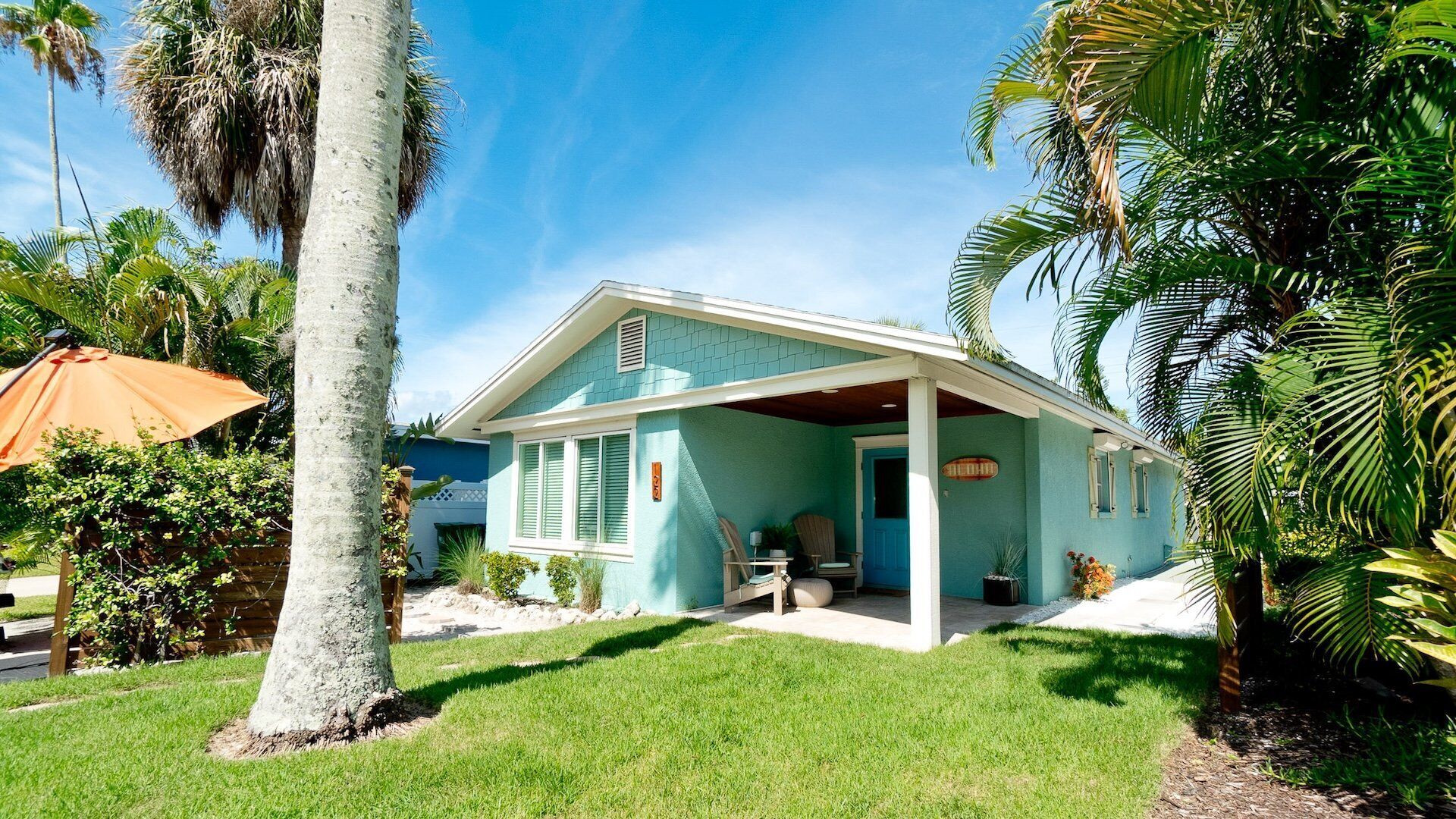 A house with a covered porch, surrounded by palm trees and a well-maintained lawn.