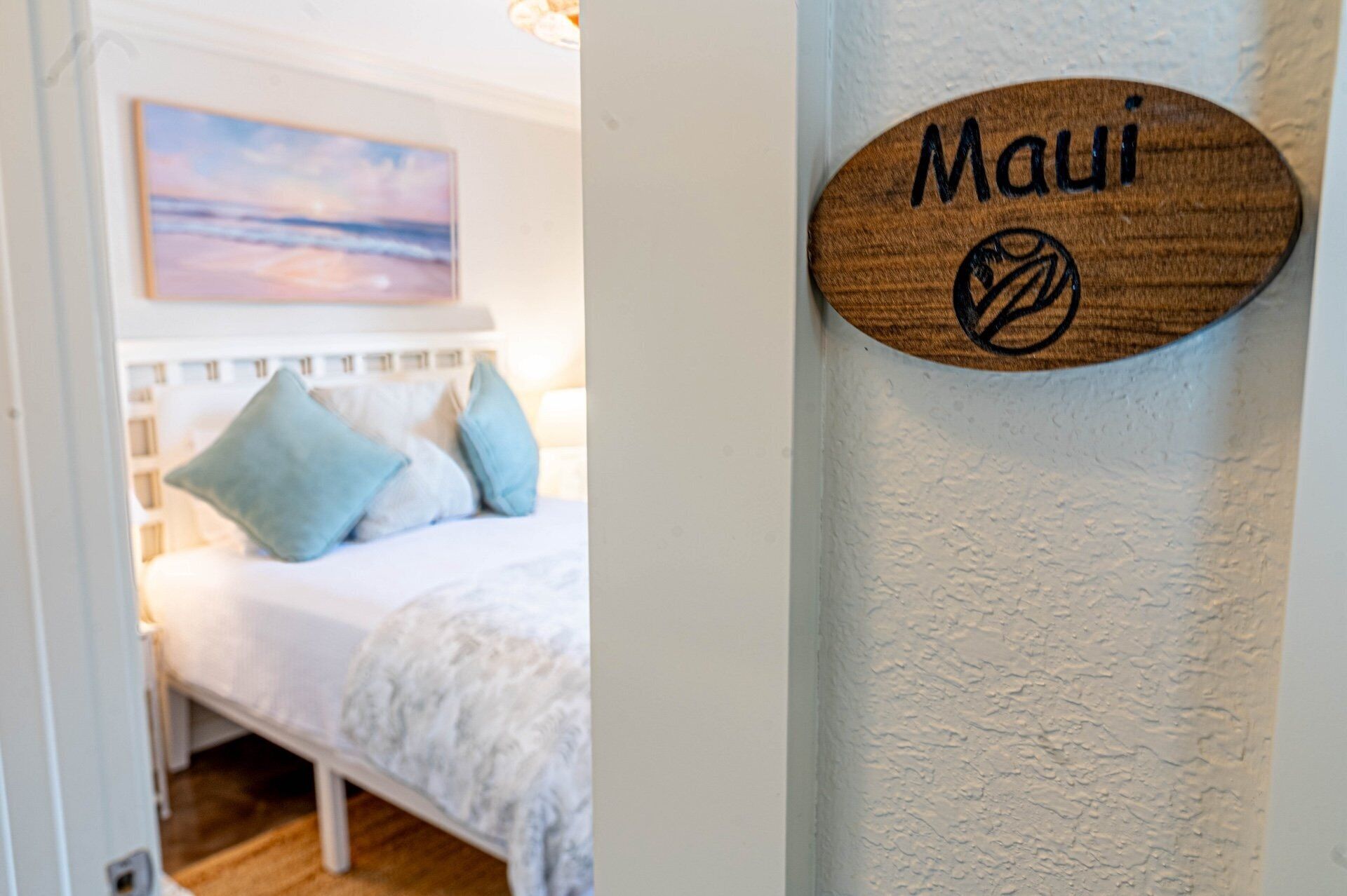Una camera da letto con un letto, cuscini e un cartello appeso al muro con su scritto "Maui".