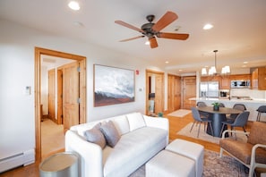 A modern living room with a white sofa, a ceiling fan, and a dining area with a round table and chairs.