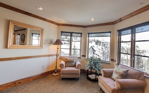 A corner room with a patterned carpet, a sofa, a chair, a lamp, and large windows with a view of a snowy landscape. - Charlie's Slopeside: Ski-In/Out, BC Village, Remodeled Kitchen + AC, Sleeps 6, Walk to Everything (Beaver Creek)