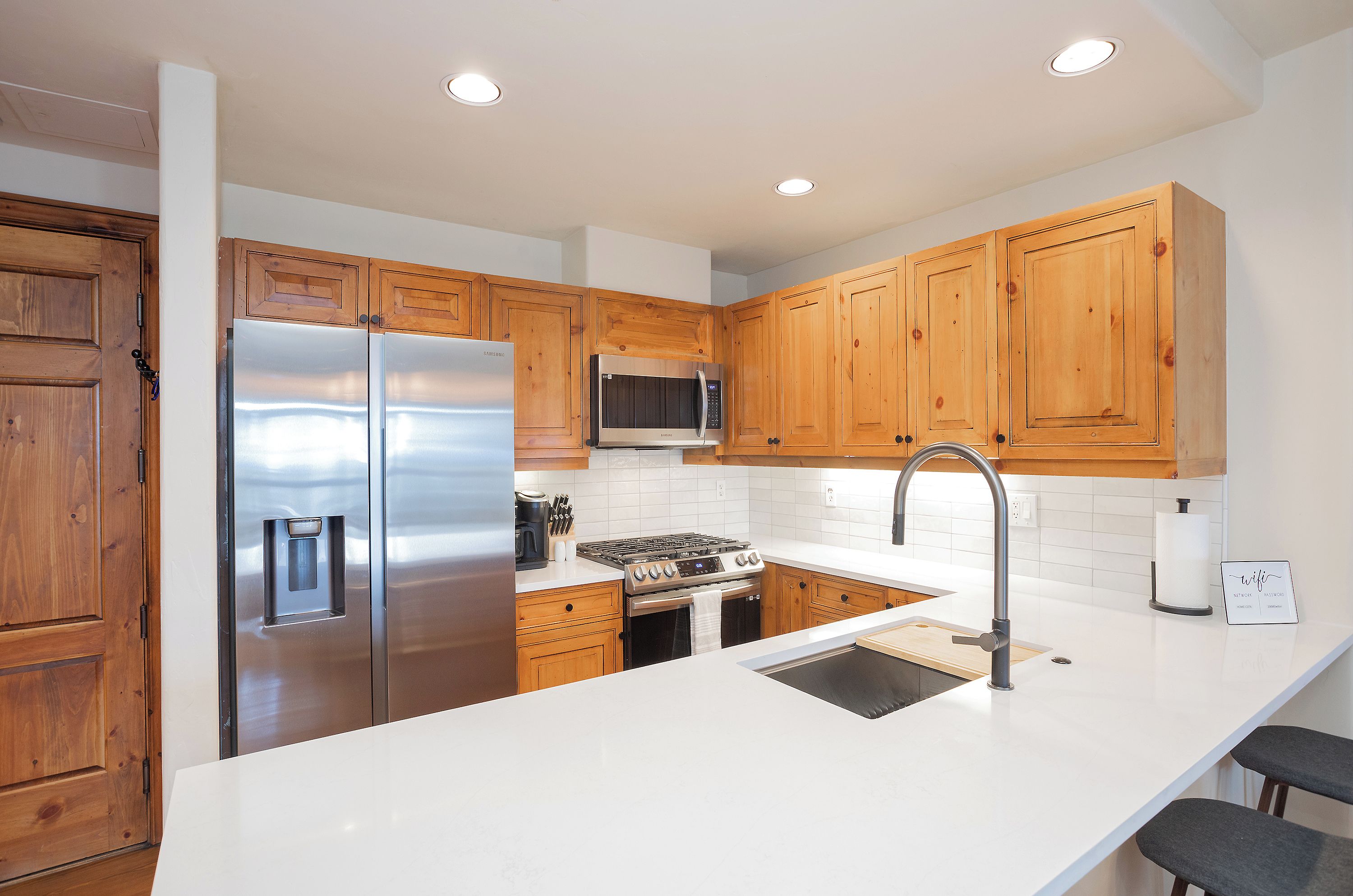 A modern kitchen with wooden cabinets, stainless steel appliances, and a white countertop.