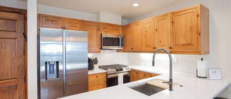 A modern kitchen with wooden cabinets, stainless steel appliances, and a white countertop.