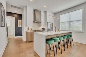 A modern kitchen with a central island, bar stools, and a large window with blinds.