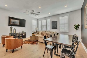 Una sala de estar moderna con sofá, sillas, una mesa de comedor y un ventilador de techo.