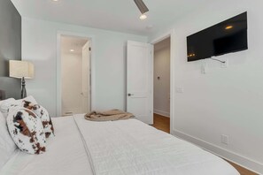Une chambre à coucher avec un lit, un téléviseur fixé au mur et une porte donnant sur une autre pièce.