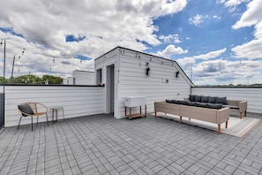 A rooftop patio with a white building, outdoor furniture, and string lights.