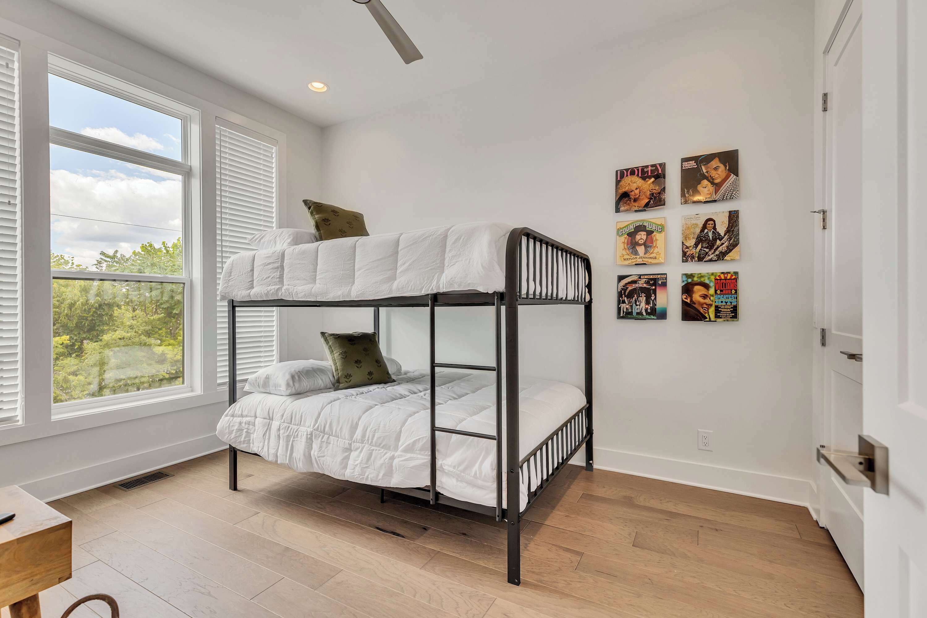 Una litera con ropa de cama blanca en una habitación con ventanas amplias, piso de madera y decoración en las paredes.