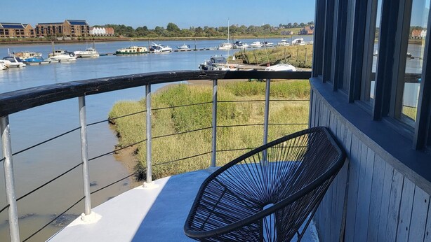 A balcony with a white table and a black chair, overlooking a marina with boats and buildings in the background. - Inner Dowsing Lightship (Rochester)