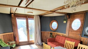 A cozy room with a wooden floor, a dining table with chairs, a red sofa, and a small black stove. - Inner Dowsing Lightship (Rochester)