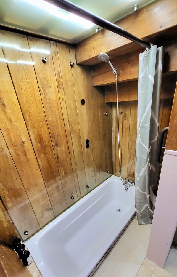 A wooden-paneled shower enclosure with a white bathtub and a showerhead. - Inner Dowsing Lightship (Rochester)