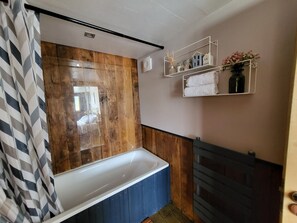 A bathroom with a wooden panel wall, a white bathtub, and a towel rack with towels.