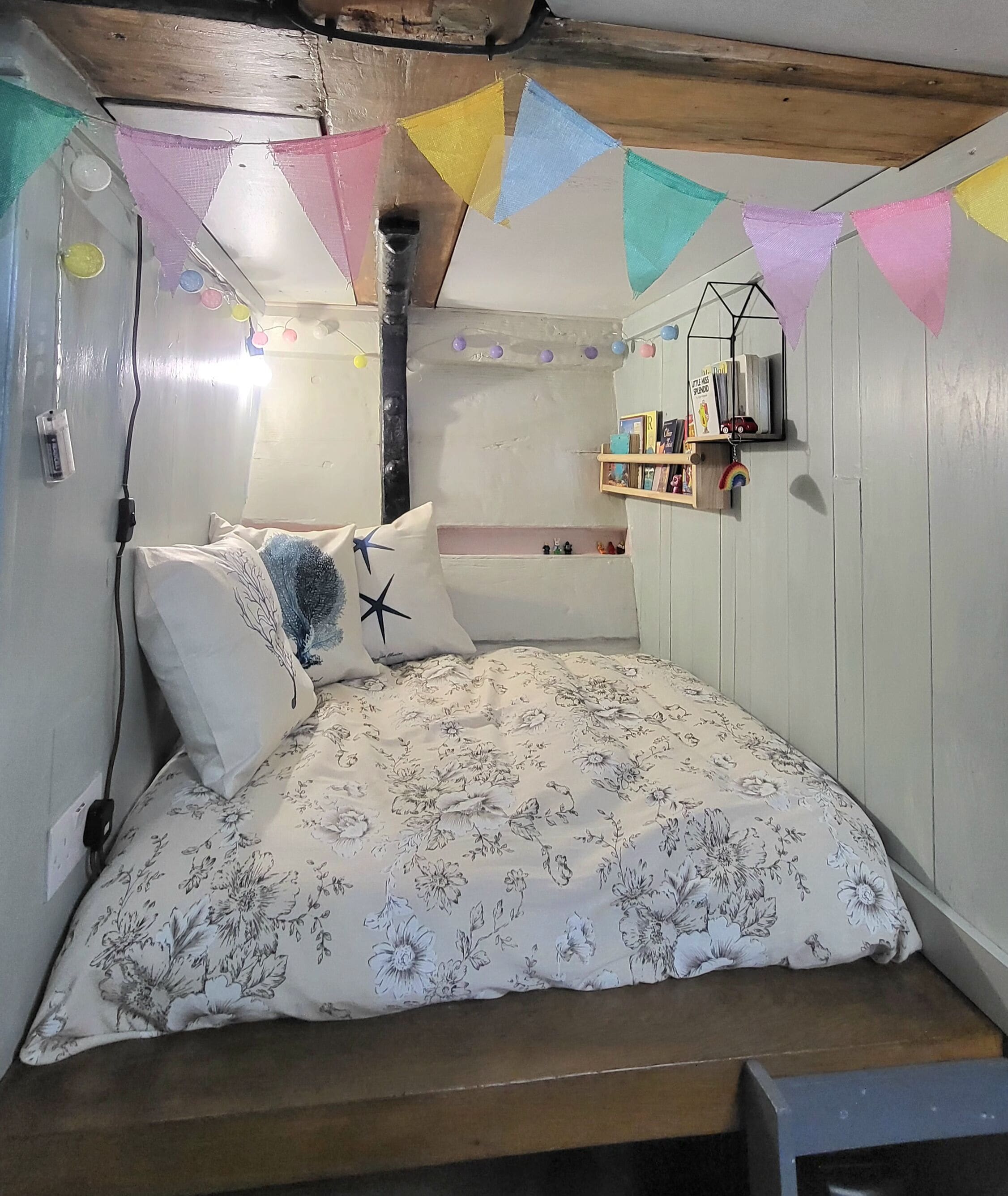 Un dormitorio acogedor con colcha estampada, cabecera de madera y estante con libros y juguetes.