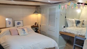 A bedroom with a large bed, a smaller bed, a desk, and a ladder. There are framed pictures on the wall and a shelf with books and a lamp. - Inner Dowsing Lightship (Rochester)
