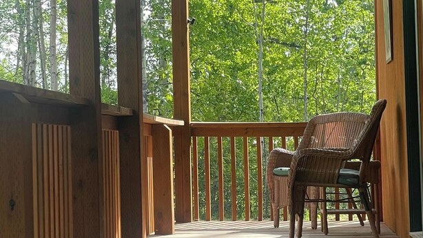 A wooden deck with a railing, wicker chairs, and a hanging planter. - Trail House, Denali Brewing, Netflix, Concert, Fire Pit, Family, Race, festival  (Talkeetna)