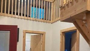 A room with a loft area, wooden doors, a red door, a white washing machine, a blue bed, and a leather couch. - Trail House, Denali Brewing, Netflix, Concert, Fire Pit, Family, Race, festival  (Talkeetna)