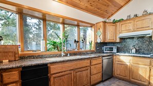 Une cuisine avec des meubles en bois, un plan de travail en granit, un lave-vaisselle, un four à micro-ondes et une fenêtre donnant sur les arbres.