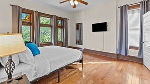 Een hotelkamer met een bed, een plafondventilator, een televisie en een raam met gordijnen.