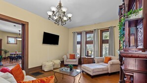 Een ruime woonkamer met een grote televisie, comfortabele zithoek, een kroonluchter en grote ramen.