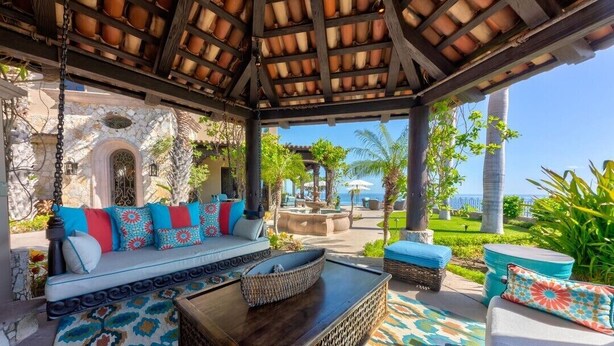 A covered outdoor seating area with a sofa, cushions, and a coffee table.