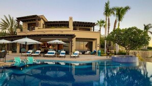 A resort with a pool, lounge chairs, umbrellas, and a view of the ocean.