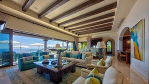 A spacious living room with a large window overlooking the sea, furnished with sofas and a coffee table.