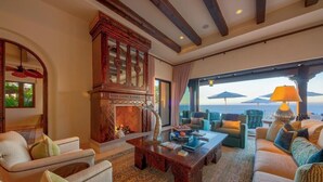 A spacious living room with a fireplace, comfortable seating, and a large window overlooking the ocean.