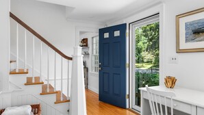 Una escalera con escalones de madera y barandillas blancas, una puerta azul con paneles de vidrio y un escritorio blanco con una silla.