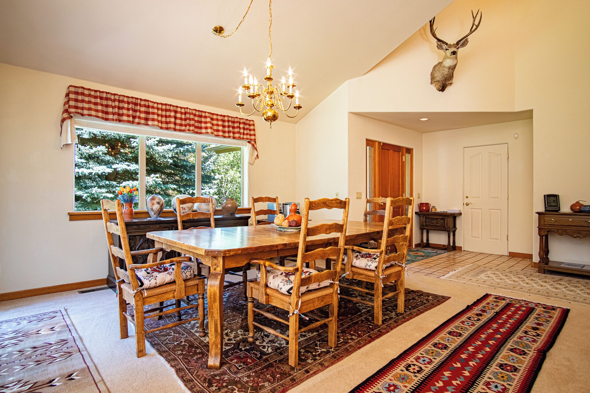 A dining room with a wooden table and chairs, a chandelier, and a deer head mounted on the wall.