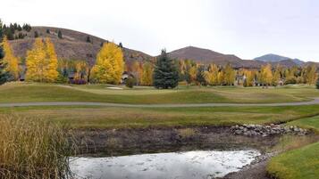 A golf course with a pond, autumn trees, and a hilly backdrop.