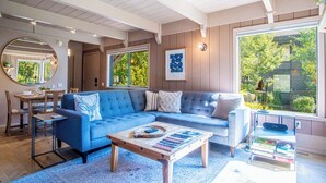 A cozy living room with a blue sofa, wooden coffee table, and a dining area with a wooden table and chairs. - Wildwood Cottage at Villager + SV Resort Amenities (Sun Valley)