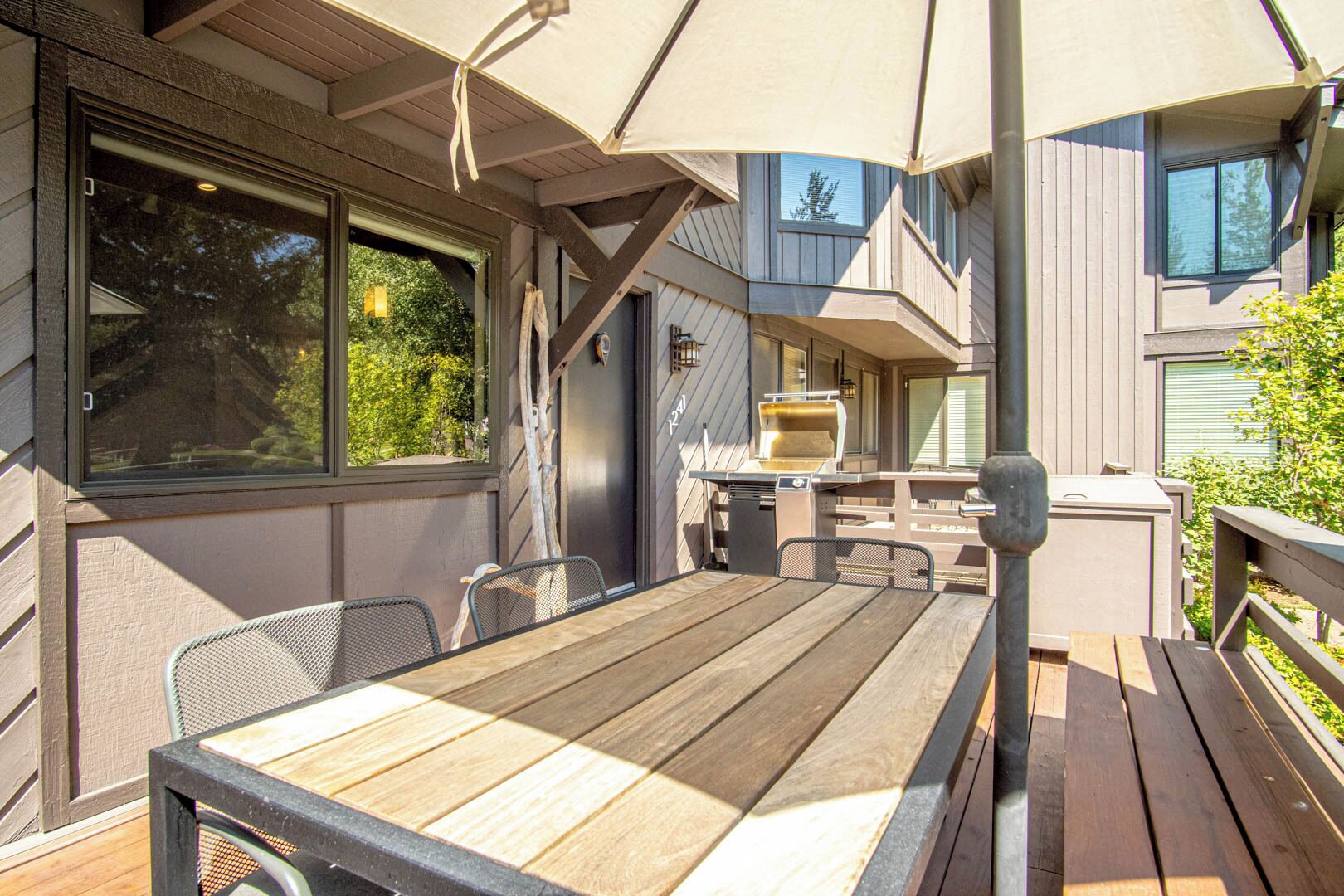 Une terrasse extérieure avec une table et des chaises en bois, un barbecue et une pergola offrant de l’ombre.