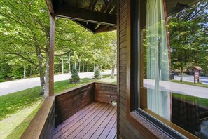 A wooden deck with a bench, a covered area, and a view of a road and trees. - Make Yourself at Home D18 (Killington)