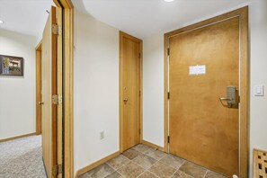 A hallway with two wooden doors, one with a visible lock and a small sign on the wall. - Make Yourself at Home D18 (Killington)