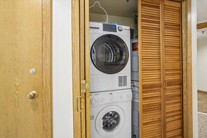 A laundry room with stacked washing machines and a wooden door. - 2 bedroom Ski-in condo with pool, hot tub, and EV chargers (Killington)