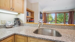 Uma cozinha com bancadas de granito, pia de aço inoxidável, armários de madeira, cafeteira e janela com cortinas.
