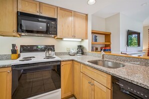 A kitchen with wooden cabinets, a microwave, stove, sink, and dishwasher. - 2 bedroom Ski-in condo with pool, hot tub, and EV chargers (Killington)