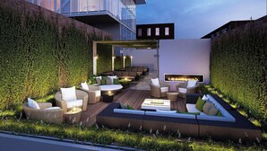 A modern outdoor lounge area with seating and a fire feature, surrounded by greenery and a glass building in the background. - Travive Brand New Four Bedroom Penthouse (New York)