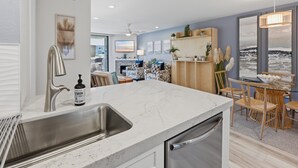 Una cocina moderna con un lavamanos de acero inoxidable, lavavajillas integrado y un comedor con mesa de vidrio y sillas de madera.