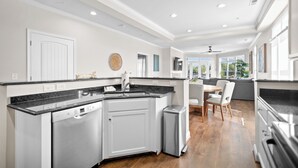 A modern kitchen with white cabinetry, a black countertop, and a dining area with a table and chairs. - Point of View by SoCharm | Luxury Lakefront Condo | Deck | Sleep 6 (Mooresville)
