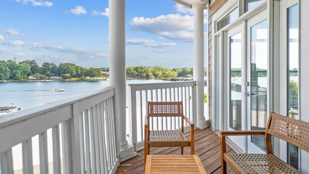 A wooden deck with white railings overlooking a body of water, a wooden chair, and a bench. - Point of View by SoCharm | Luxury Lakefront Condo | Deck | Sleep 6 (Mooresville)