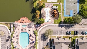 An aerial view of a resort with a swimming pool, sun loungers, a basketball court, and a tennis court.