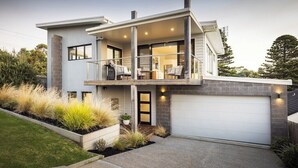A modern two-story house with a covered balcony, a garage, and landscaped garden beds.