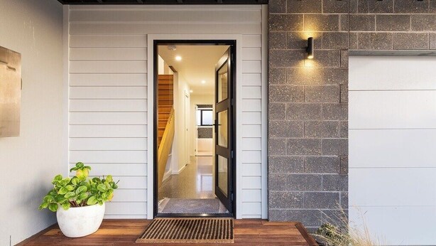 A modern entrance with a wooden floor, a potted plant, and a stone wall.