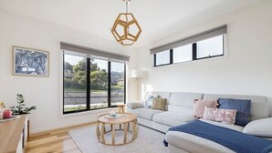 A modern living room with a sofa, a round wooden coffee table, and a large window providing a view of the outdoors.