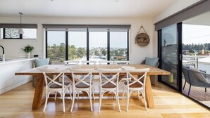 A modern dining area with a wooden table and white chairs, large windows with a view, and a balcony with outdoor seating.