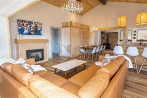 Uma sala de estar espaçosa com lareira, sofás de couro, área de jantar com parede de tijolos e cozinha com luminárias pendentes.