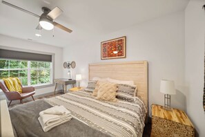 A modern bedroom with a large bed, a desk, a chair, and a ceiling fan.
