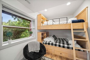 Quarto com beliche, janela, cadeira pequena e armário de madeira.